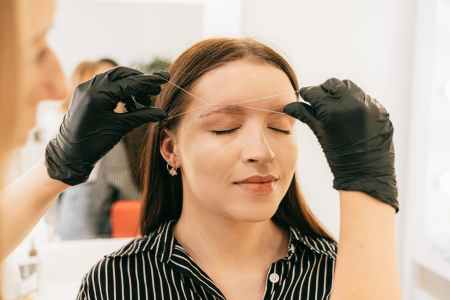 woman in black and white striped shirt getting an eyebrow threading