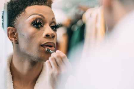 ethnic transgender applying makeup on lips