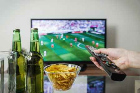Person watching football match with beers and snacks