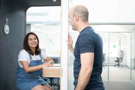 a person sitting on a call booth talking to a coworker at the office