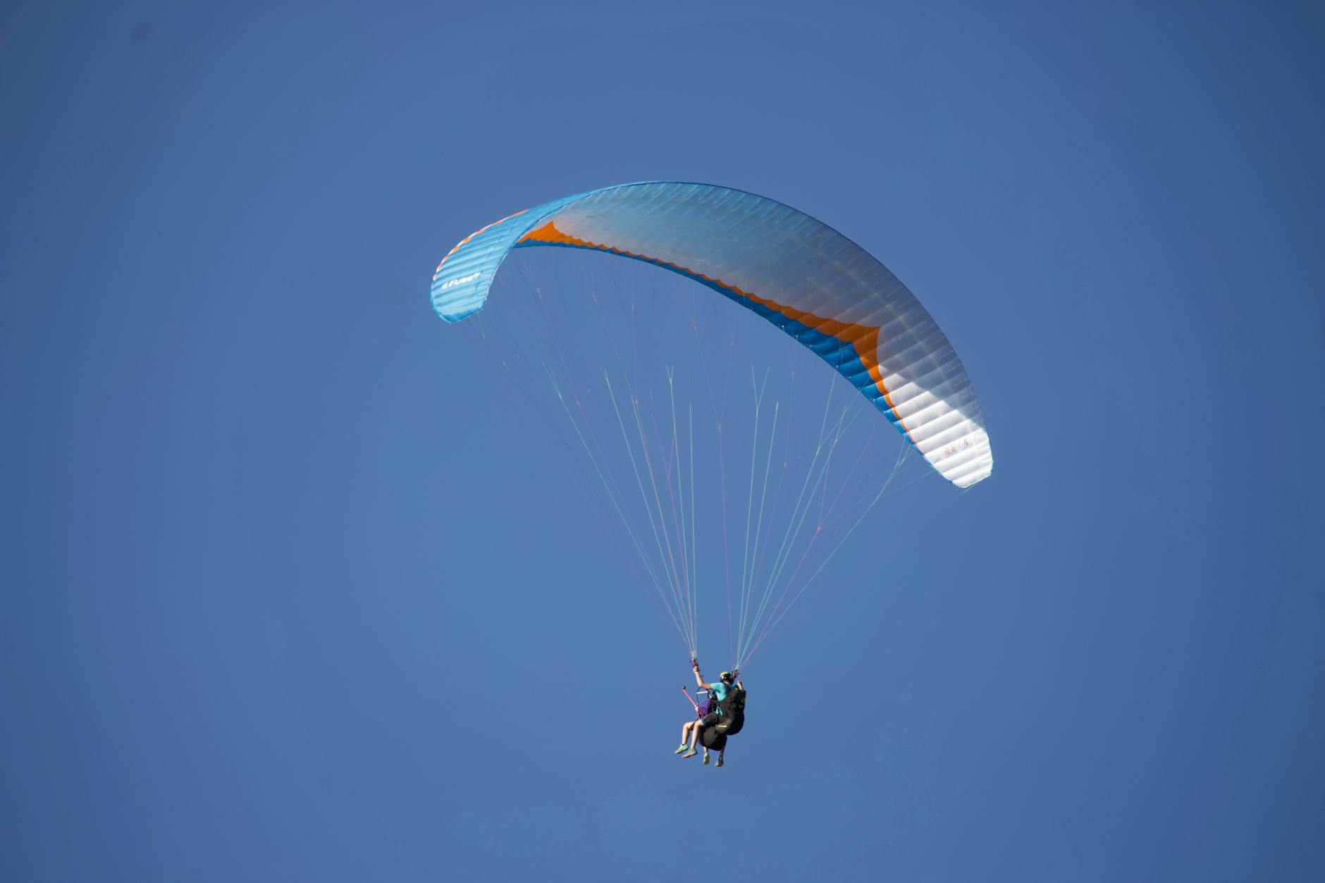 anonymous paraglider flying in blue sky